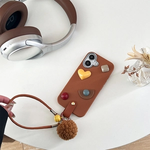 Brown leather phone case with 3D heart shapes, hand strap, bell, and plush ball detail