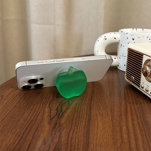 Green apple-shaped expanding cell phone grip stand on a white smartphone on wooden desk