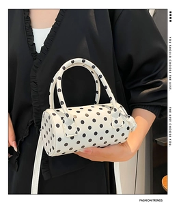 Dettaglio di una borsa a cilindro bianca a pois neri con manici e tracolla alla moda