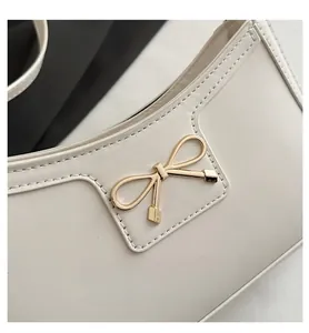 Detailed view of cream leather baguette bag with a golden bow metal accessory and stitching
