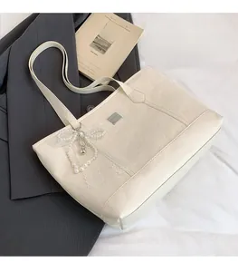 Détail du sac fourre-tout crème avec logo en relief et breloque nœud en perles et dentelle