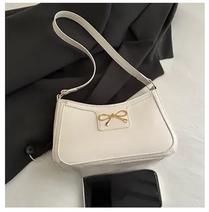 Detail of a creamy white underarm bag with a golden bow buckle and smooth leather texture