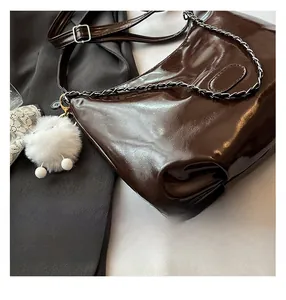 Detail of dark brown glossy leather tote bag with metallic chain and white pompom charm