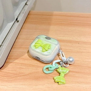 Sparkly green AirPods case with 3D bow and pearl keychain on a wooden surface