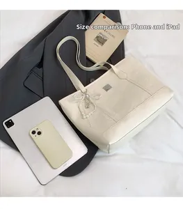 Vue de capacité du sac cabas crème avec nœud perlé montrant un iPad pour comparer la taille