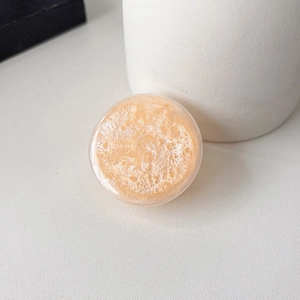 Close-up of a peach orange round phone grip with glitter and shiny sequins on a clean background