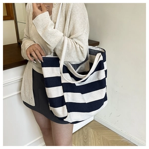 Close-up of a large striped canvas tote bag in navy and beige worn on the shoulder