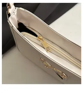 Detailed close-up of smooth gold zipper and bow buckle on minimalist white shoulder bag