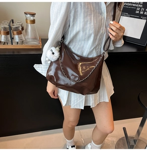 Brown glossy tote bag with silver chain and cute plush dog charm shown in a cafe setting