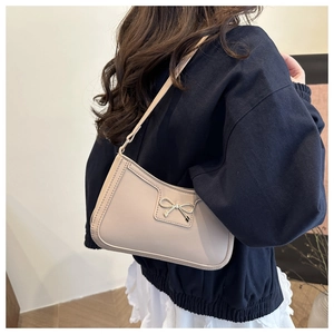 Detail of a chic beige underarm bag with a decorative silver metal bow on smooth leather
