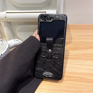 Détail de la coque pliante en cuir noir avec nœud et logo argenté sur bois