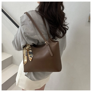 Detailed view of brown tote bag with contrast stitching and floral silk scarf charm