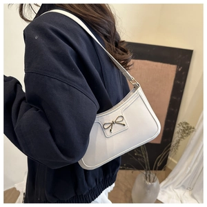 Detail shot of a white underarm bag featuring a delicate golden metal bow clasp detail
