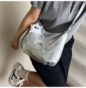 Detail of silver metallic crossbody bag with chain and white plush doll on stairs