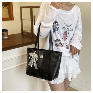 Détail du sac cabas noir gaufré avec un nœud en dentelle blanche et un pendentif perle