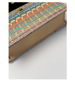 Macro detail of the rainbow woven flap and gold magnetic clasp on the straw clutch bag