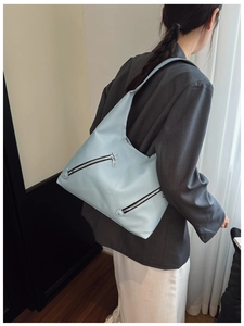 Detail of light blue tote bag with lychee grain texture and diagonal zippers on shoulder