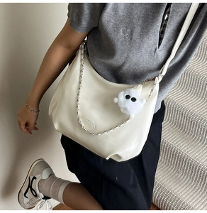 Detail of creamy white crescent hobo bag with metal chain and plush monster charm