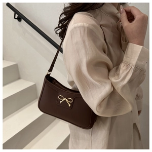 Brown underarm bag with gold bow detail shown on a model in a minimalist setting