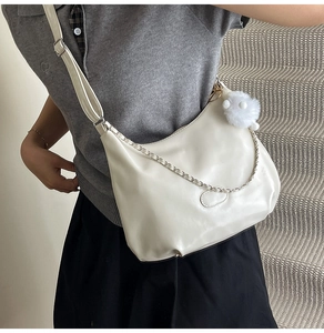 Detail of white crescent crossbody bag with silver chain and plush charm on a model