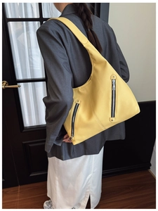 Side view of a bright yellow pebbled leather tote bag with dual zipper pockets on a model