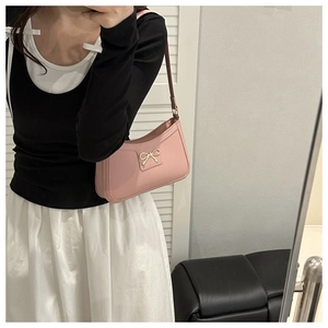 Detailed close-up of a pink leather underarm bag with a golden bow and slim shoulder strap