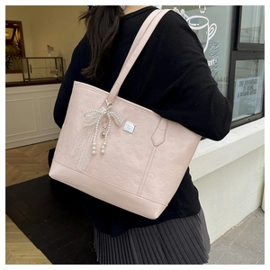 Détail d'un sac cabas rose avec motifs embossés et pendentif nœud en perles