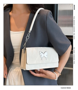 Detail of white pleated underarm bag featuring a silver butterfly buckle and chain strap