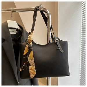 Detail of a black textured tote bag with a patterned silk scarf on a chrome hanger