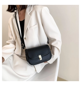 Détail d'un petit sac bandoulière en cuir mat noir avec boucle dorée sur un blazer blanc