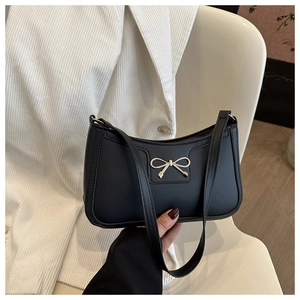 Detail of elegant black shoulder bag featuring a decorative golden bow and matte leather finish
