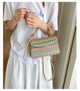 Detail of woven straw crossbody bag featuring colorful wave patterns and a knotted handle