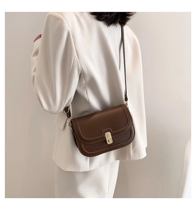 Gros plan d'un sac bandoulière vintage en cuir marron avec boucle en métal sur un blazer blanc