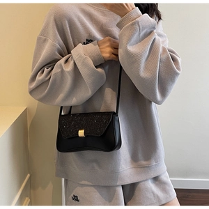 Detail of a black textured crossbody bag with a gold buckle worn on a grey waffle outfit