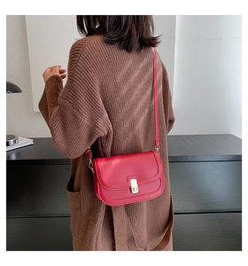 Détail du sac à bandoulière vintage rouge avec boucle dorée sur un mannequin en pull marron