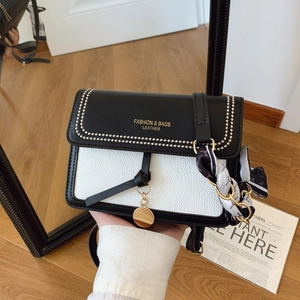 Detailed shot of black and white crossbody bag with gold chain and printed silk scarf