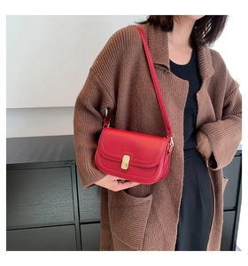 Gros plan d'un sac besace rouge vintage avec boucle dorée sur un gilet marron