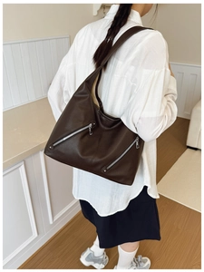 Detail of dark brown tote bag showing textured leather surface and silver zipper pockets
