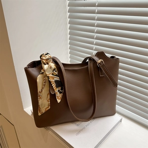 Brown leather tote bag with contrast stitching and decorative scarf in soft window light