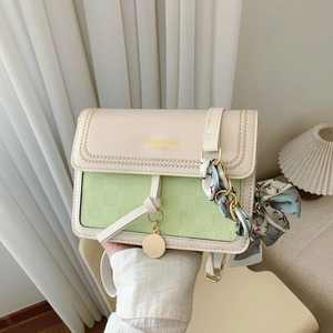 Detail of crossbody bag featuring green contrast flap, silk scarf handle, and gold charm