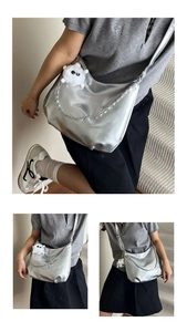 Detail of silver metallic crescent tote bag featuring a metal chain and plush monster charm