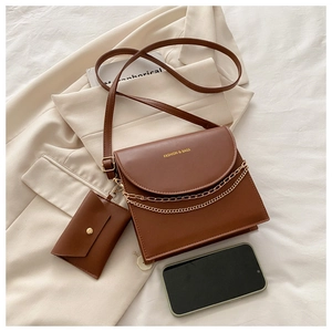 Détail d'un sac bandoulière marron avec chaîne dorée et mini pochette sur tissu beige
