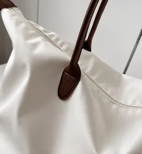 Primer plano detallado del bolso de viaje blanco de nailon con asas de cuero marrón resistentes