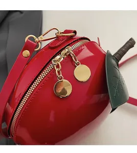 Détail du sac pomme rouge en cuir verni montrant le zip doré et l'ornement feuille