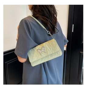Detail of pistachio green pleated handbag with silver butterfly clasp shown on shoulder