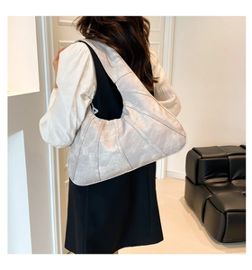 Detailed view of light gray hobo bag with radial stitching on minimalist model shoulder
