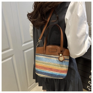 Close-up of a colorful woven bucket bag with brown leather trim and golden metal zippers