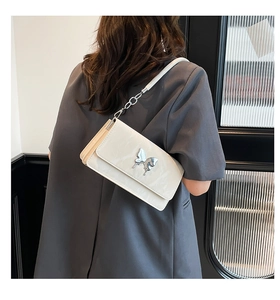 Detail view of the white square bag featuring a silver butterfly clasp on a female model
