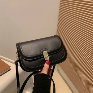 Sac à bandoulière minimaliste en similicuir noir avec fermoir doré sur fond de bois