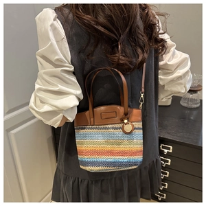 Detail of colorful woven straw bucket bag with brown leather handles and gold metal charm